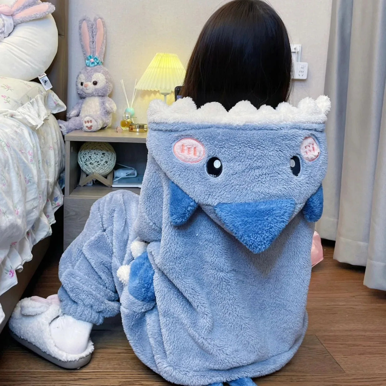 Person wearing a blue dinosaur-themed robe in a room with stuffed animals.