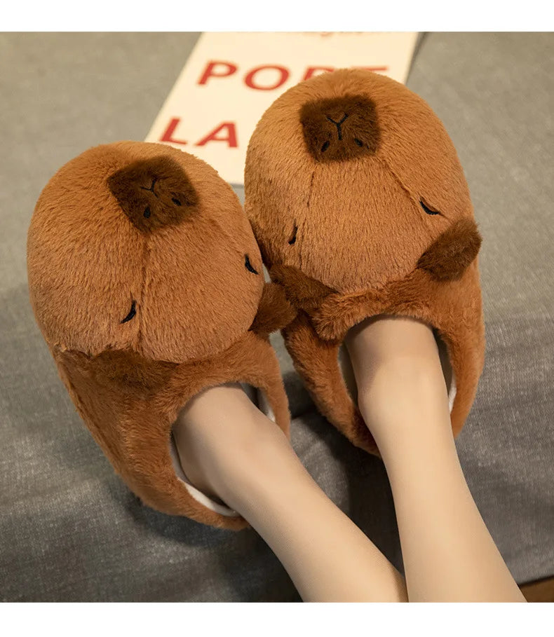 Brown plush slippers with bear face design worn by a person on a gray surface.