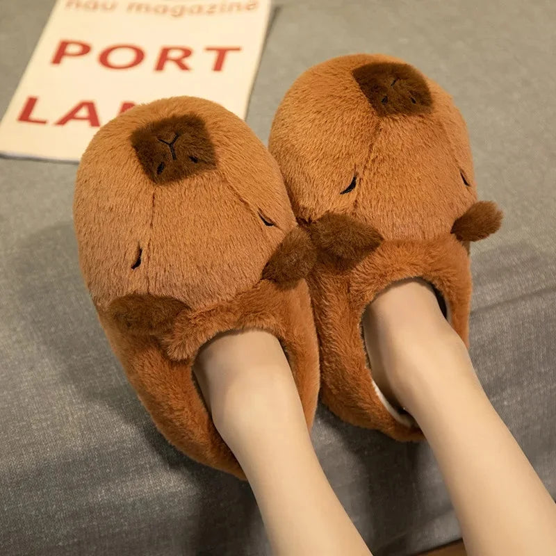 Brown plush slippers with a face design worn by a person on a gray surface.