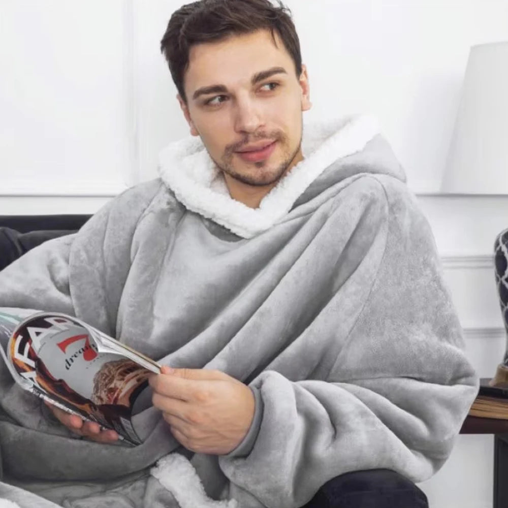Man wrapped in a gray blanket reading a magazine indoors.