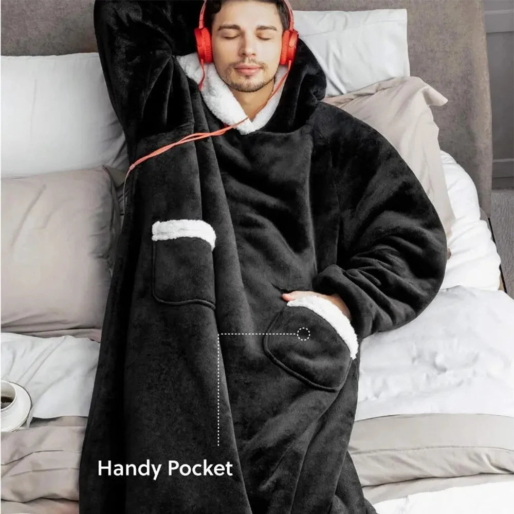 Person wearing a black hoodie with a pocket, sitting on a bed with headphones on.